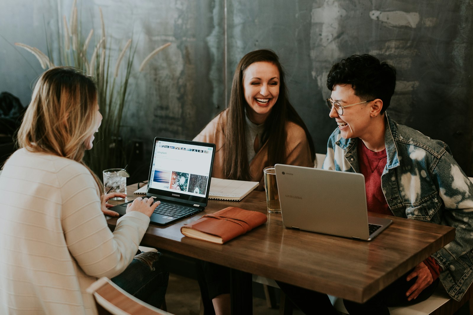 Drei Fachleute lachen beim Überprüfen von Arbeit an Laptops